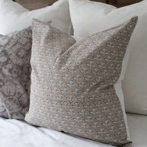 May include: Three decorative throw pillows on a white bed. The pillows are made of a soft, textured fabric. One pillow has a floral pattern, one has a geometric pattern, and one is plain white.