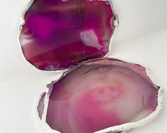 May include: Two pink agate coasters with a silver trim. The coasters are made of natural stone and have a unique, organic shape.