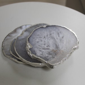May include: Set of four agate coasters with a silver trim. The coasters are white with grey veining and have a natural, organic shape.