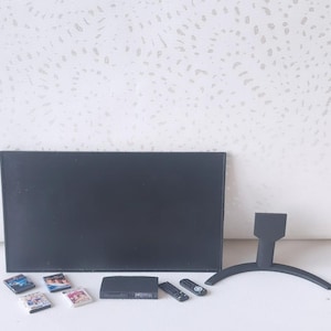 May include: Miniature black television with a stand, a DVD player, two remote controls, and several DVD cases. The TV is rectangular and has a sleek design. The DVDs have colorful covers. The stand has a curved base.