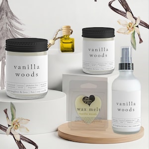 May include: A collection of Vanilla Woods scented products, including candles, a room spray, and wax melts. The products are in clear glass jars and bottles with black lids and labels. The wax melts are heart-shaped.