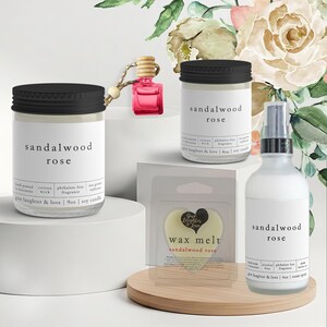 May include: A collection of sandalwood rose scented products, including candles, wax melts, and room spray. The products are in clear glass jars and bottles with black lids and labels. The image includes a small pink car air freshener.