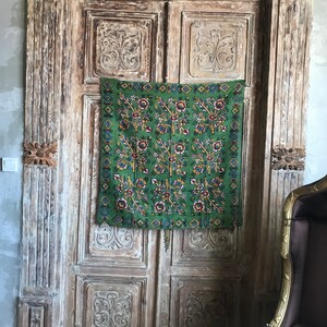 May include: A green floral tapestry with a yellow, red, and blue pattern hangs on a weathered wooden door with intricate carvings.