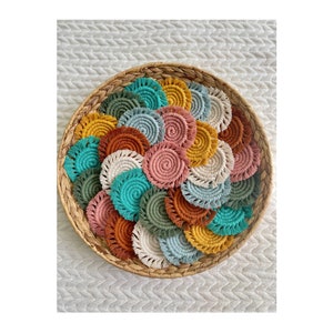 May include: A wicker basket filled with colorful round crocheted coasters with fringe. The coasters are in shades of blue, green, pink, orange, and white.