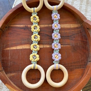 May include: Two wooden rings with macrame flower accents. The rings are natural wood and the flowers are in shades of yellow, green, and purple.