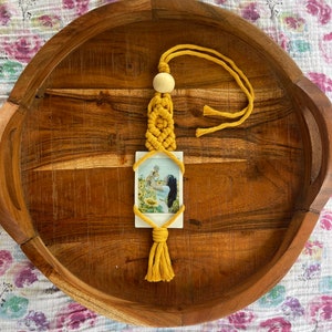 May include: A yellow macrame photo holder with a wooden bead and a tassel. A photo of a woman and a child in a sunflower field is displayed in the holder.