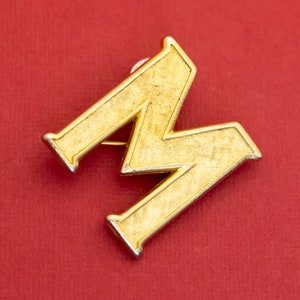 Broche vintage con letra M en tono dorado - F34