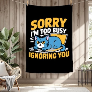 Puede incluir: Tapiz negro con el texto "SORRY I'M TOO BUSY IGNORING YOU". El diseño presenta un gato azul con expresión enfadada, sentado frente a un portátil amarillo. El texto es en amarillo y blanco.