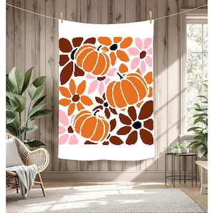 May include: White rectangular throw blanket with a repeating pattern of orange pumpkins and flowers in shades of brown, pink, and black. The blanket is hanging from a clothesline against a wooden wall.