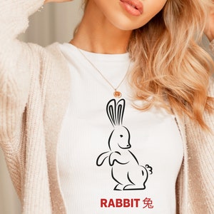以下が含まれることがあります： ウサギの黒い線画が描かれた白いTシャツ。ウサギの下に「RABBIT 兔」という文字が印刷されています。