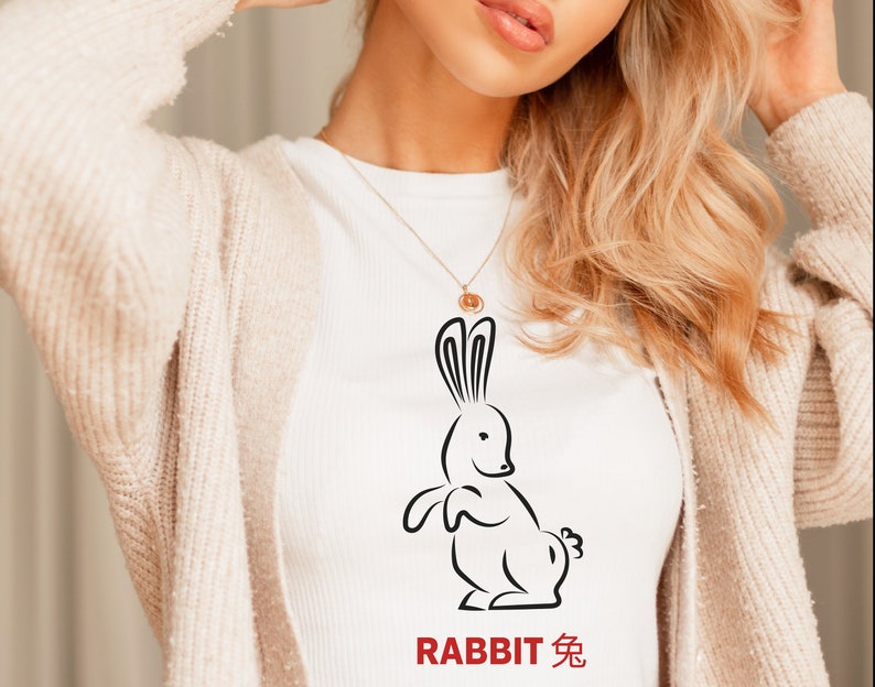 以下が含まれることがあります： ウサギの黒い線画が描かれた白いTシャツ。ウサギの下に「RABBIT 兔」という文字が印刷されています。