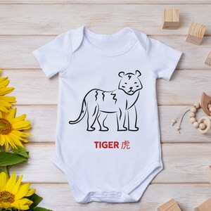 以下が含まれることがあります： 虎の線画と赤い文字「TIGER 虎」が描かれた白いベビーロンパース