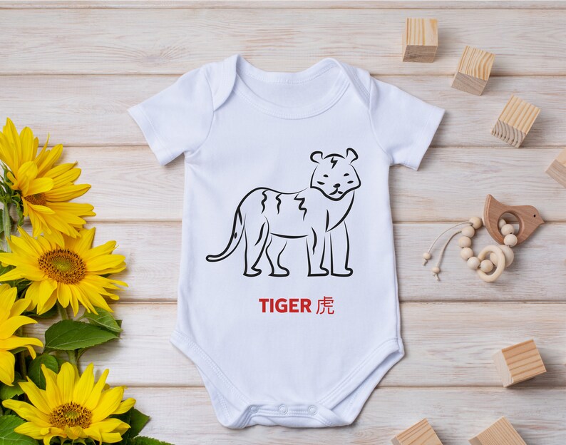 以下が含まれることがあります： 虎の線画と赤い文字「TIGER 虎」が描かれた白いベビーロンパース
