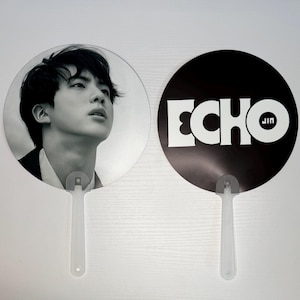 May include: Two black and white hand fans. One fan features a black and white photo of a person. The other fan has the word "ECHO" in white letters with "JIN" in smaller white letters on a black background.