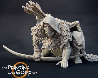 May include: A detailed miniature figurine of a hooded figure with a bow and arrow, dressed in a cloak with leaves and branches, in a crouching pose. The figure is painted in a light beige color.