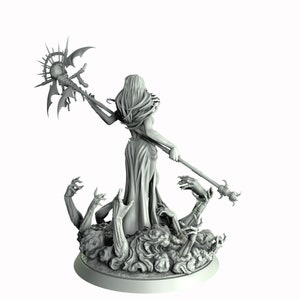 May include: A gray painted miniature figurine of a female figure with long hair, wearing a flowing robe and holding a staff with a sun-like orb at the top. The figure is standing on a base with multiple skeletal hands reaching up.