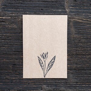 May include: A blank brown card with a black floral design printed on it. The card is sitting on a dark wood surface.