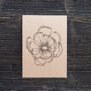 May include: A simple line drawing of a flower on a brown card.