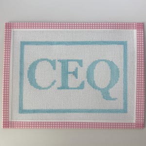 May include: A rectangular needlepoint canvas with a white background, a light blue border, and the letters "CEQ" in light blue. The border is framed with a pink and white gingham pattern.