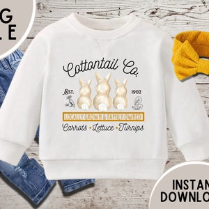 Puede incluir: Sudadera blanca de manga larga con un gráfico de conejo marrón y el texto "Cottontail Co. Est. 1902 Locally Grown & Family Owned Carrots Lettuce Turnips".