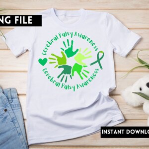 Puede incluir: Camiseta blanca con un dise&ntilde;o de huellas de manos verdes y amarillas y el texto "Cerebral Palsy Awareness". El dise&ntilde;o incluye un coraz&oacute;n verde y una cinta verde.
