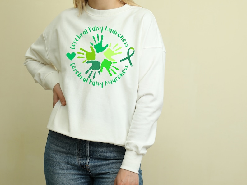 Puede incluir: Sudadera blanca con una cinta verde y huellas de manos en un c&iacute;rculo. El texto "Cerebral Palsy Awareness" est&aacute; escrito alrededor del c&iacute;rculo.