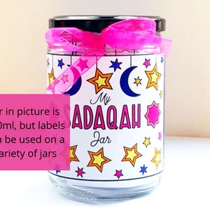May include: A clear glass jar with a pink ribbon and a white label that says "My Sadaqah Jar". The label has a crescent moon and stars in various colors. The jar is 500 ml, but the labels can be used on a variety of jars.