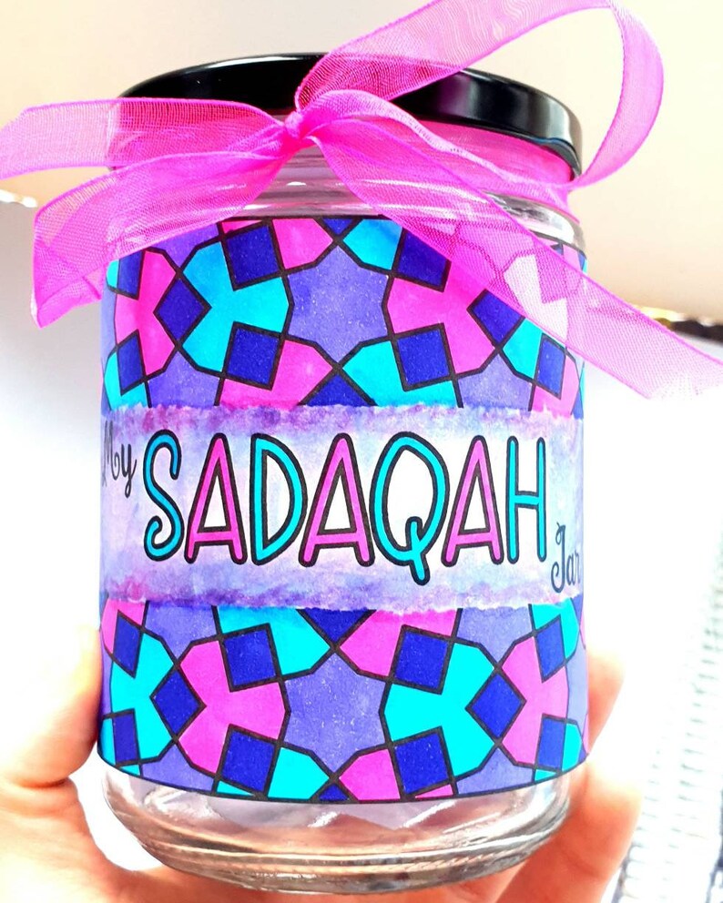 May include: A glass jar with a pink ribbon and a label that says "My Sadaqah Jar". The jar has a geometric pattern in shades of pink, blue, and purple.