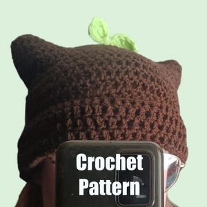 Può includere: Cappello a uncinetto marrone con un dettaglio a foglia verde. Il cappello è realizzato con un semplice punto a maglia e ha una vestibilità morbida. Modello all'uncinetto.