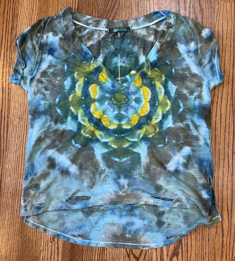 May include: A blue, green, and yellow tie-dye t-shirt with a distressed, cropped hem. The shirt has a V-neck and a circular design in the center.