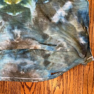 May include: A blue, green, and brown tie-dye shirt with a distressed look. The shirt has a few small holes and a frayed edge.