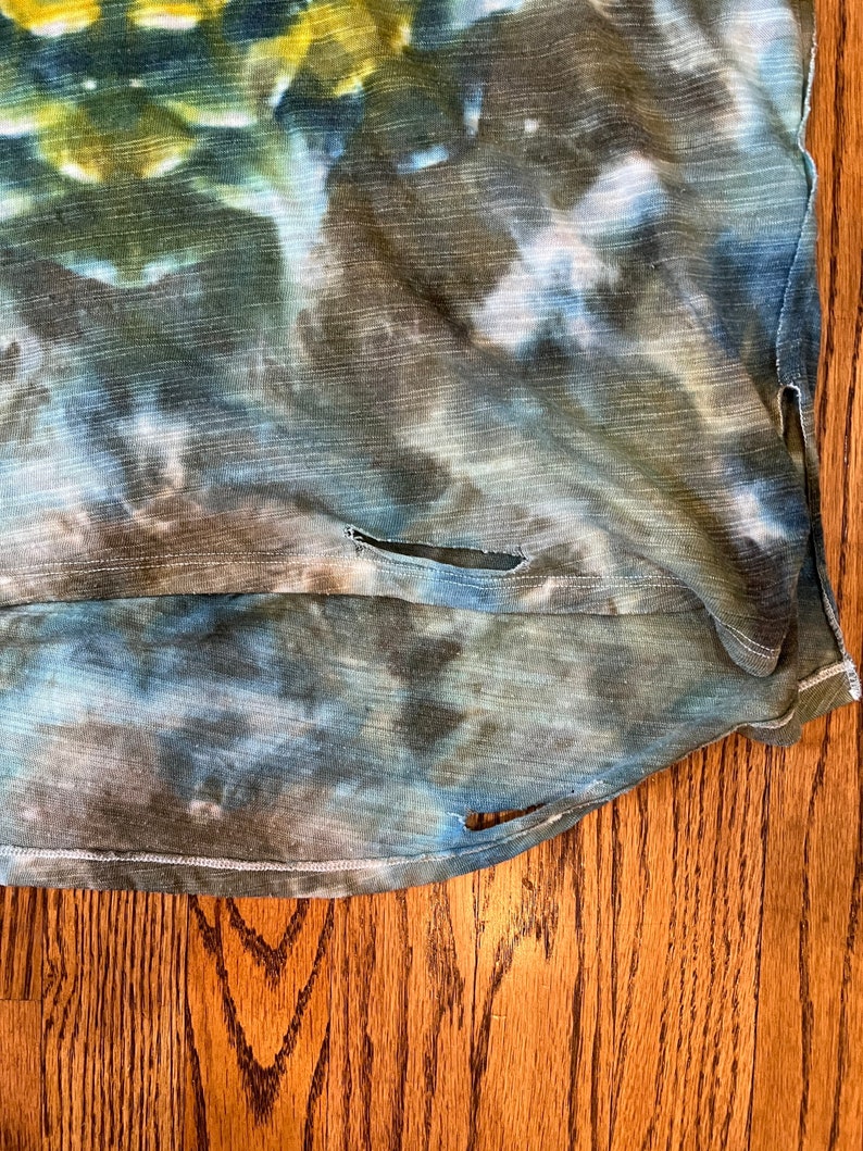 May include: A blue, green, and brown tie-dye shirt with a distressed look. The shirt has a few small holes and a frayed edge.