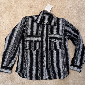 May include: A black and gray striped button-down shirt with two chest pockets. The shirt features a geometric pattern and a collar. The long-sleeved shirt is made of a textured fabric.