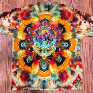 May include: A tie-dye t-shirt with a colorful mandala pattern. The shirt features a graphic of a mountain scene with the text "Dead & Co. Tour 2021".