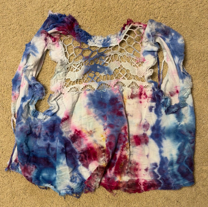 Puede incluir: Una camiseta te&ntilde;ida con un panel trasero de encaje blanco. La camisa presenta una mezcla de colores azul, rosa y blanco. Las mangas est&aacute;n recortadas y los bordes deshilachados. La camiseta est&aacute; hecha de una tela suave y ligera.