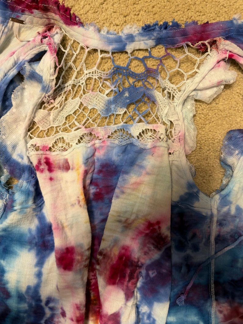 Puede incluir: Una blusa te&ntilde;ida con un panel trasero de crochet blanco. La blusa presenta una mezcla de colores azul, rosa y blanco. La tela tiene un dise&ntilde;o de borde deshilachado y deshilachado. La blusa est&aacute; hecha de un material ligero.