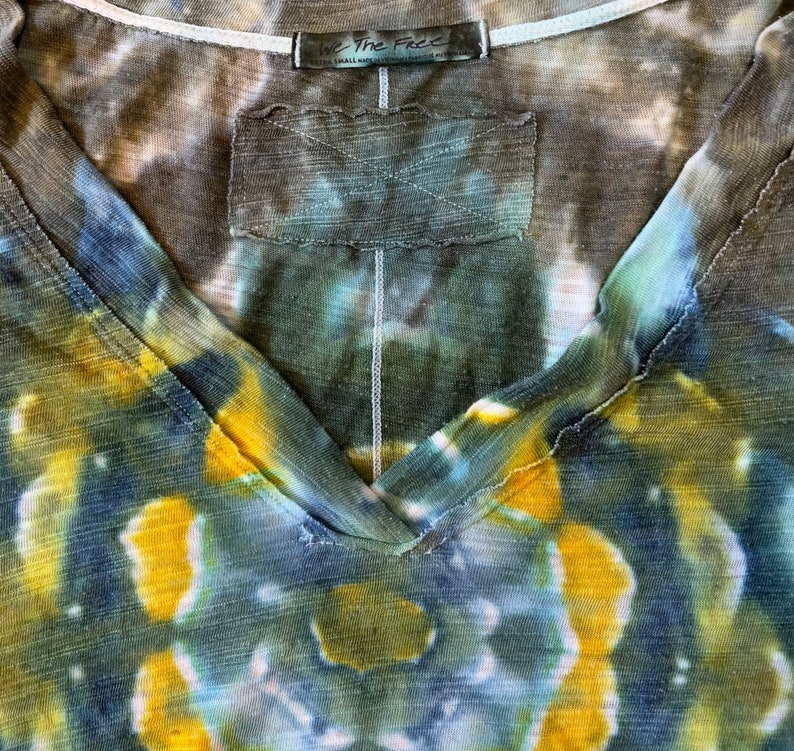 May include: A tie-dye V-neck shirt in shades of blue, green, and yellow with a brown tag that reads "We The Free" and "Extra Small Made in India" in white text.