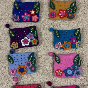May include: Nine felt coin purses with floral embroidery and beaded accents. Each purse has a different color and floral design. The purses are arranged in three rows of three.
