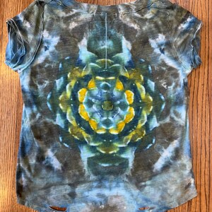 May include: A blue, green, and yellow tie-dye t-shirt with a circular pattern in the center. The shirt has a distressed look with frayed edges and holes.