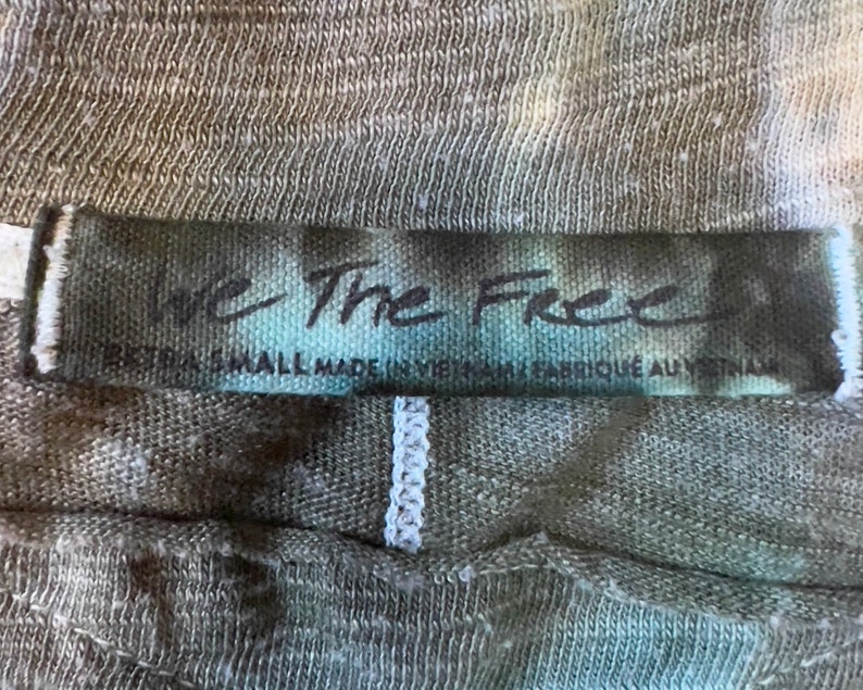 May include: A close-up of a dark green and white tie-dye shirt tag with the text "We The Free" and "Small Made in Vietnam - Fabrique au Vietnam".