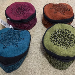 May include: Four round fabric hats with black trim and a mandala design. The hats are in shades of red, orange, green, and blue.