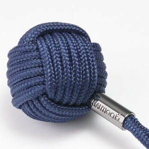 Può includere: Un portachiavi in corda blu navy con una palla annodata e un'etichetta in metallo argentato che dice "NAUTICA".