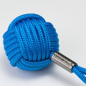 以下が含まれることがあります： 明るい青色の結び目のロープキーホルダー。シルバーの金属タグには「NAUTICA」と刻印され、シルバーの金属製のキーリングが付いています。