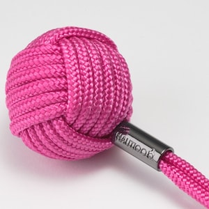 以下が含まれることがあります： シルバーのキーリングが付いた、鮮やかなピンク色のモンキーフィストキーホルダー。 結び目は、編み込みコードと「NAUTICO」の文字がプリントされた金属チューブに接続されています。