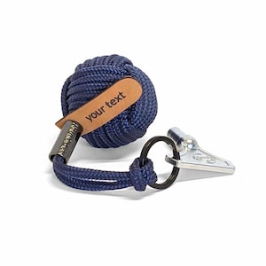 Può includere: Un portachiavi in corda blu navy con un'etichetta in pelle che dice "your text". Il portachiavi ha un anello portachiavi argentato e un fischietto argentato.