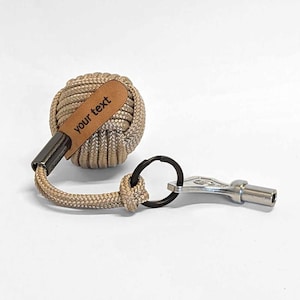 Op de afbeelding: Een beige touwtjes sleutelhanger met een leren label waarop "your text" staat en een zilveren sleutelring.