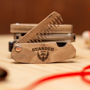 May include: A wooden beard comb with a folding design. The comb has a brown wood finish and features the text "The Bearded Man" with a beard icon.