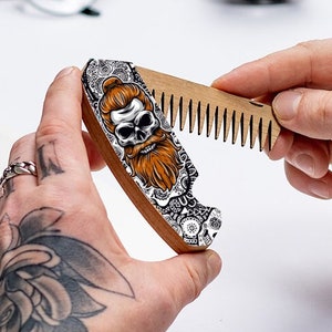 Peut inclure: Un peigne en bois avec un motif de crâne et de barbe. Le peigne est décoré de détails complexes et présente un schéma de couleurs noir et blanc.