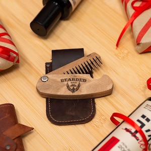 May include: A wooden pocket comb with a leather case. The comb has a wood-burned design that says "The Bearded Man" with a beard silhouette.