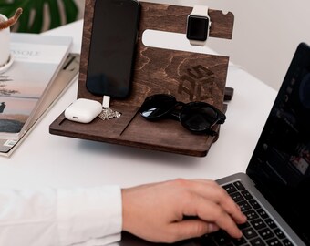May include: A wooden phone stand with a charging station for a smartphone, wireless earbuds, and a smartwatch. The stand also has a slot for sunglasses. The stand is brown and has a geometric design.